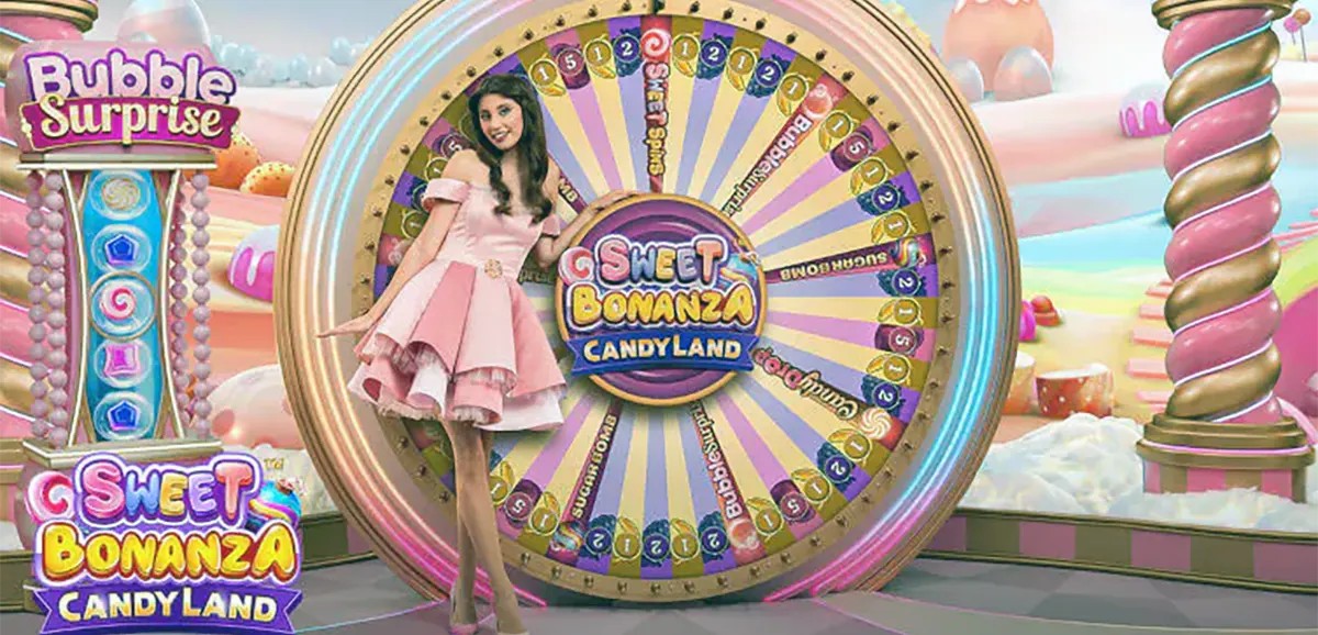 “A presenter in a pink dress poses beside the large Sweet Bonanza CandyLand bonus wheel on a colorful candy-themed game show set with pastel clouds and confectionery decorations.”